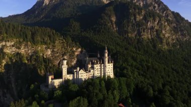 Neuschwanstein kalesi, yemyeşil ve yüksek dağların arasına kurulmuş mimari ihtişam ve doğal güzelliğin nefes kesici bir görüntüsünü sunar.