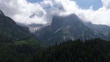 İsviçre 'nin en yüksek dağı olan marmolada buzulunun görkemli hava manzarası kalın bulutlar ve bir vadideki yemyeşil kozalaklı ormanla çevrili.