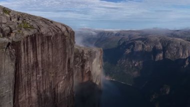 Kjerag Dağı 'nın katıksız granit yamaç yüzeyi, Lysefjord' un derin mavi sularının üzerinde yükselirken, yaylada kısa bir süre görülebilen bir yürüyüşçü ile hayranlık uyandırıcı bir hava manzarası.