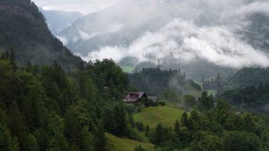 Alçak asılı bulutlar yemyeşil dağlık vadide yavaşça sürükleniyor, Avustralya kırsalındaki sakin atmosferik koşullara sahip yemyeşil manzaraların arasına yerleşmiş izole edilmiş dağ evini ortaya çıkarıyor.