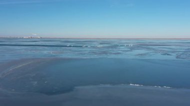 Güneşli bir kış gününde donmuş Hazar Denizi 'nde buz kütleleri arasında yüzen zarif beyaz kuğu sürüsünün güzel hava perspektifi. Arka planda uzak bir şehir kıyı şeridi görünüyor