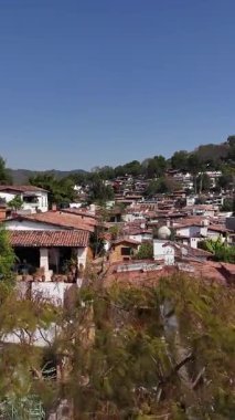 Meksika 'nın tarihi Valle de Bravo kasabasının geleneksel kırmızı kiremit çatıları ve beyaz binaları üzerinde uçan yüksek açılı hava görüntüleri yemyeşil bir vadiye yerleşmiştir.