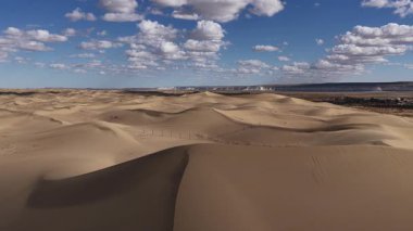 Mangystau, Kazakistan 'daki uçsuz bucaksız çöl kum tepeleri üzerinde alçaktan uçan inanılmaz hava manzarası, dağınık bulutlarla dolu güzel mavi gökyüzü altında karmaşık dokularını ve kıvrımlarını ortaya çıkarıyor.