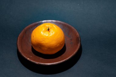 Tahta tabakta taze portakal meyvesi, siyah zemin üzerinde izole edilmiş Dekopon portakalı ya da iş yolu üzerinde sumo mandalina..