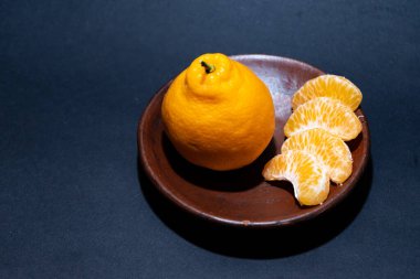 Tahta tabakta taze portakal meyvesi, siyah zemin üzerinde izole edilmiş Dekopon portakalı ya da iş yolu üzerinde sumo mandalina..