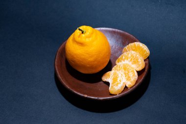 Tahta tabakta taze portakal meyvesi, siyah zemin üzerinde izole edilmiş Dekopon portakalı ya da iş yolu üzerinde sumo mandalina..