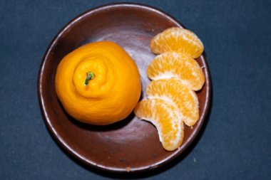 Tahta tabakta taze portakal meyvesi, siyah zemin üzerinde izole edilmiş Dekopon portakalı ya da iş yolu üzerinde sumo mandalina..