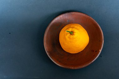 Tahta tabakta taze portakal meyvesi, siyah zemin üzerinde izole edilmiş Dekopon portakalı ya da iş yolu üzerinde sumo mandalina..