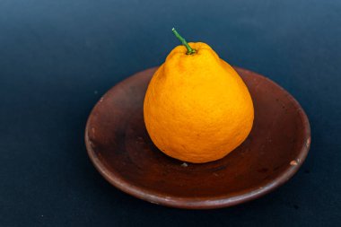 Tahta tabakta taze portakal meyvesi, siyah zemin üzerinde izole edilmiş Dekopon portakalı ya da iş yolu üzerinde sumo mandalina..