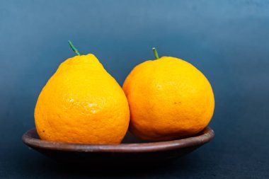 Tahta tabakta taze portakal meyvesi, siyah zemin üzerinde izole edilmiş Dekopon portakalı ya da iş yolu üzerinde sumo mandalina..