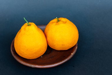 Tahta tabakta taze portakal meyvesi, siyah zemin üzerinde izole edilmiş Dekopon portakalı ya da iş yolu üzerinde sumo mandalina..