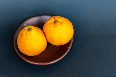 Tahta tabakta taze portakal meyvesi, siyah zemin üzerinde izole edilmiş Dekopon portakalı ya da iş yolu üzerinde sumo mandalina..