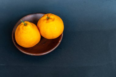 Tahta tabakta taze portakal meyvesi, siyah zemin üzerinde izole edilmiş Dekopon portakalı ya da iş yolu üzerinde sumo mandalina..