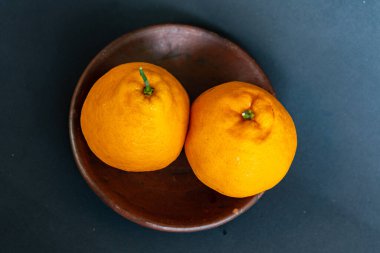 Tahta tabakta taze portakal meyvesi, siyah zemin üzerinde izole edilmiş Dekopon portakalı ya da iş yolu üzerinde sumo mandalina..