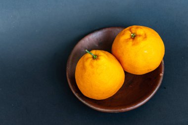 Tahta tabakta taze portakal meyvesi, siyah zemin üzerinde izole edilmiş Dekopon portakalı ya da iş yolu üzerinde sumo mandalina..