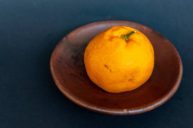 Tahta tabakta taze portakal meyvesi, siyah zemin üzerinde izole edilmiş Dekopon portakalı ya da iş yolu üzerinde sumo mandalina..