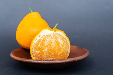 Tahta tabakta taze portakal meyvesi, siyah zemin üzerinde izole edilmiş Dekopon portakalı ya da iş yolu üzerinde sumo mandalina..