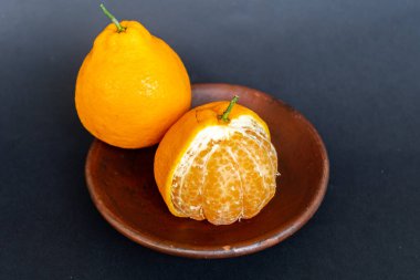 Tahta tabakta taze portakal meyvesi, siyah zemin üzerinde izole edilmiş Dekopon portakalı ya da iş yolu üzerinde sumo mandalina..