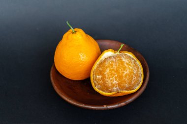 Tahta tabakta taze portakal meyvesi, siyah zemin üzerinde izole edilmiş Dekopon portakalı ya da iş yolu üzerinde sumo mandalina..