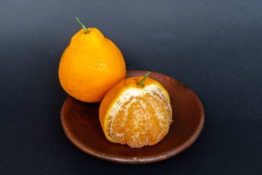 Tahta tabakta taze portakal meyvesi, siyah zemin üzerinde izole edilmiş Dekopon portakalı ya da iş yolu üzerinde sumo mandalina..