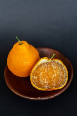 Tahta tabakta taze portakal meyvesi, siyah zemin üzerinde izole edilmiş Dekopon portakalı ya da iş yolu üzerinde sumo mandalina..