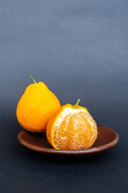 Tahta tabakta taze portakal meyvesi, siyah zemin üzerinde izole edilmiş Dekopon portakalı ya da iş yolu üzerinde sumo mandalina..
