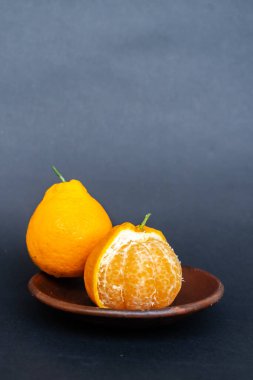 Tahta tabakta taze portakal meyvesi, siyah zemin üzerinde izole edilmiş Dekopon portakalı ya da iş yolu üzerinde sumo mandalina..
