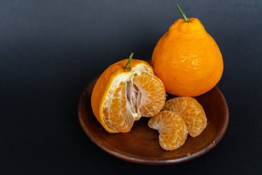 Tahta tabakta taze portakal meyvesi, siyah zemin üzerinde izole edilmiş Dekopon portakalı ya da iş yolu üzerinde sumo mandalina..