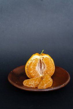 Tahta tabakta taze portakal meyvesi, siyah zemin üzerinde izole edilmiş Dekopon portakalı ya da iş yolu üzerinde sumo mandalina..