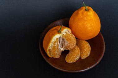 Tahta tabakta taze portakal meyvesi, siyah zemin üzerinde izole edilmiş Dekopon portakalı ya da iş yolu üzerinde sumo mandalina..