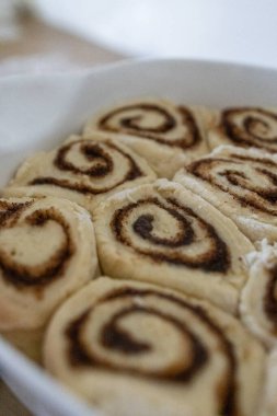 Mutfak masasında seramik bir tabakta pişirilmiş taze ev yapımı tarçın ruloları. Sıcak altın kabuk, sarmal doku, tatlı tatlı konsepti, sıcak ev yapımı atmosfer..