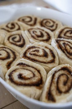 Mutfak masasında seramik bir tabakta pişirilmiş taze ev yapımı tarçın ruloları. Sıcak altın kabuk, sarmal doku, tatlı tatlı konsepti, sıcak ev yapımı atmosfer..