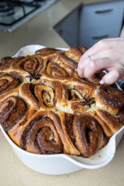 Mutfak masasında seramik bir tabakta pişirilmiş taze ev yapımı tarçın ruloları. Sıcak altın kabuk, sarmal doku, tatlı tatlı konsepti, sıcak ev yapımı atmosfer..