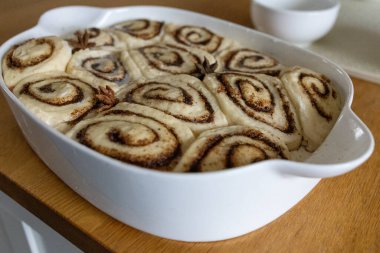 Mutfak masasında seramik bir tabakta pişirilmiş taze ev yapımı tarçın ruloları. Sıcak altın kabuk, sarmal doku, tatlı tatlı konsepti, sıcak ev yapımı atmosfer..