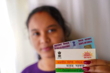 Beyaz arka planda PAN ve Aadhaar kartları tutan Hintli bir kadın seçici odaklı ya da sığ alan derinliğinde.