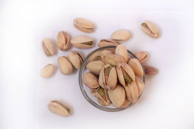 Cam bir kaseye tuzlu şam fıstığı serpiştirilmiş ve beyaz bir zemine saçılmış, yalıtılmış, yan görünüm, kızarmış fındık, lezzetli, besleyici aperatif, sağlıklı organik gıda, yüksek proteinli vejetaryen bileşeni.