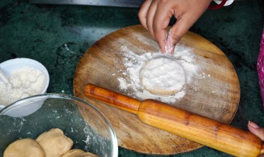Hamur kadar yakın çekim. Elleri ahşap masada merdaneyle hamuru pişiriyor. Genç Hintli kadın elleri, masanın üzerinde un ve fırında pişirme arkaplanı olan oklavaya devam ediyor..