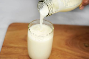 Beyaz bir masanın üzerine cam bardağa süt dökmek. Süt şişesinde çiftlikten alınmış inek sütü. Beyaz arkaplan.