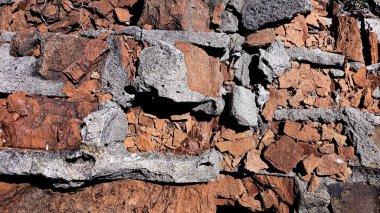 Kırmızımsı kayalar ve gri havan topuyla sert taş duvar..