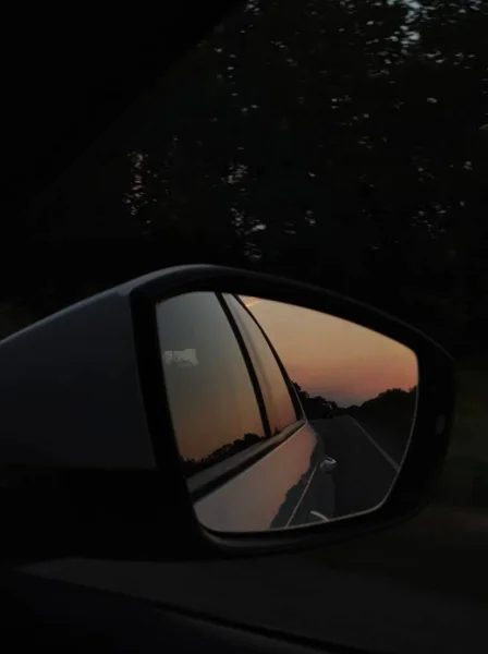 Huzurlu bir günbatımı araba yan aynası ve penceresine yansıyarak, ağaçlık bir yolda huzurlu bir yolculuk yakalıyor, seyahat ve otomotiv teması için ideal..