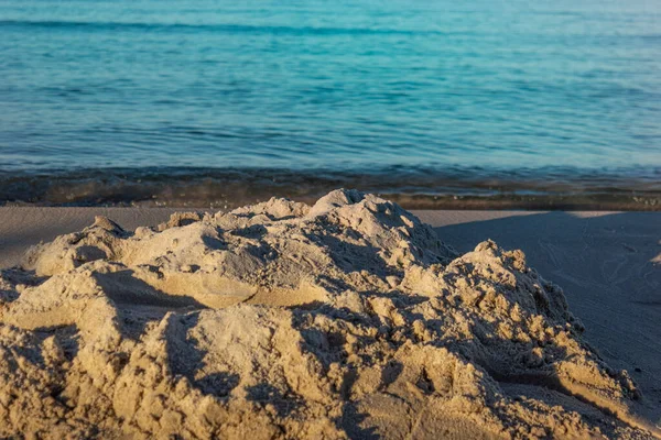 Islak Baltık Denizi sahillerinde doğa tarafından yontulmuş desenli kum yığınının yakın çekimi, yumuşak altın gün batımı ışığında turkuaz dalgalar, sakin kıyı dokusu