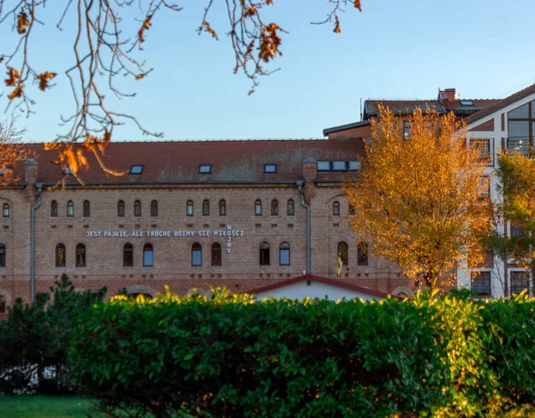 Ustka şehrinde sonbahar ağaçları ve altın günbatımı ışığı tarafından çerçevelenmiş, beyaz harflerle Lehçe alıntılanmış, tarihi kırmızı tuğla bina cephesi. Motivasyon, şehir keşfi, Polonya kültürü için harika.