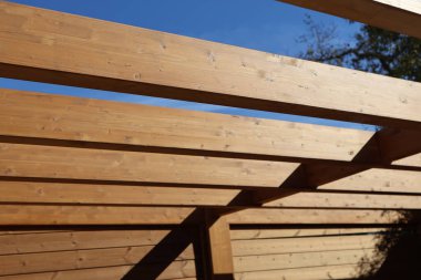 Pergola 'nın ahşap kirişleri açık hava alanları için mükemmel, açık mavi gökyüzüne karşı güzel bir desen oluşturur.