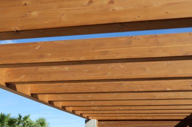 Pergola 'nın ahşap kirişleri mavi gökyüzüne karşı güzel bir desen oluşturuyor. Gölge ve stil sunuyor.