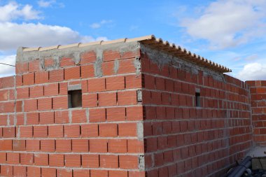 Kırmızı tuğla yapı, kısmen tamamlanmış çatı ve pencere açıklıklarıyla inşaatın ilk safhalarında yer alıyor.