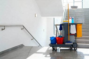 Arkasında merdiven olan bir bina koridorunda bir temizlik arabası kullanıma hazır.