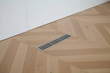 Bu görüntüde şık bir ringa kemiği ahşap zemin, parlak metal bir menfez ve beyaz bir duvar var.