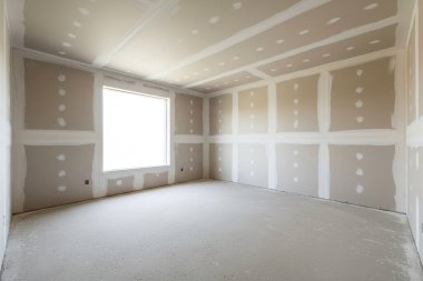 Bu görüntü, inşaat aşamasında bir odanın içini gösteriyor, alçıpan ve tamamlanmamış bir zemin içeriyor.