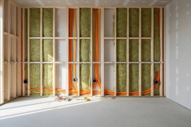 Görüntü inşaat sırasında bir duvarın içini gösteriyor, açıkta kalan kablolar, ahşap çerçeve ve izolasyon