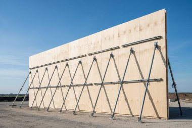 Büyük ahşap bir duvar metal kirişlerle desteklenerek inşaat alanında güçlü ve istikrarlı bir yapı oluşturulur.